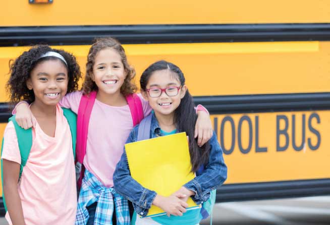 Three students standing in front of a yellow school bus